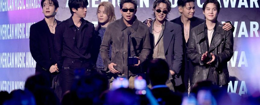 Czterech mężczyzn stoi na scenie w eleganckich strojach, trzymając nagrodę, w tle napisy AMERICAN MUSIC AWARDS.