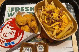 Obraz przedstawia zestaw fast food: nuggetsy, frytki z serem i sosem, podane na tacy.