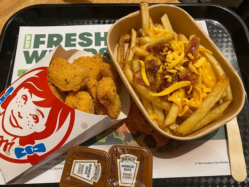 Obraz przedstawia zestaw fast food: nuggetsy, frytki z serem i sosem, podane na tacy.