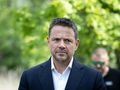 Mężczyzna w garniturze na tle zieleni, z poważnym wyrazem twarzy. Nie znam jego tożsamości.
