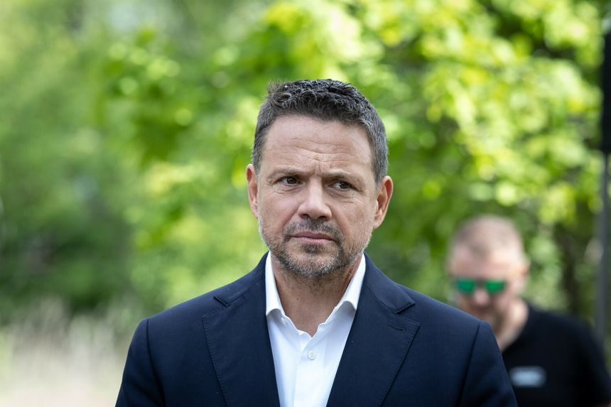 Mężczyzna w garniturze na tle zieleni, z poważnym wyrazem twarzy. Nie znam jego tożsamości.