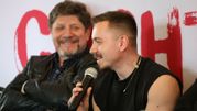 Na zdjęciu mężczyzna z mikrofonem w ręku, obok uśmiechający się mężczyzna w skórzanej kurtce.