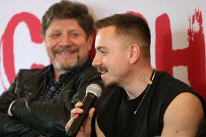 Na zdjęciu mężczyzna z mikrofonem w ręku, obok uśmiechający się mężczyzna w skórzanej kurtce.