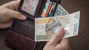 Zdjęcie przedstawia dłoń trzymającą banknot 200 zł w portfelu z kartami płatniczymi.