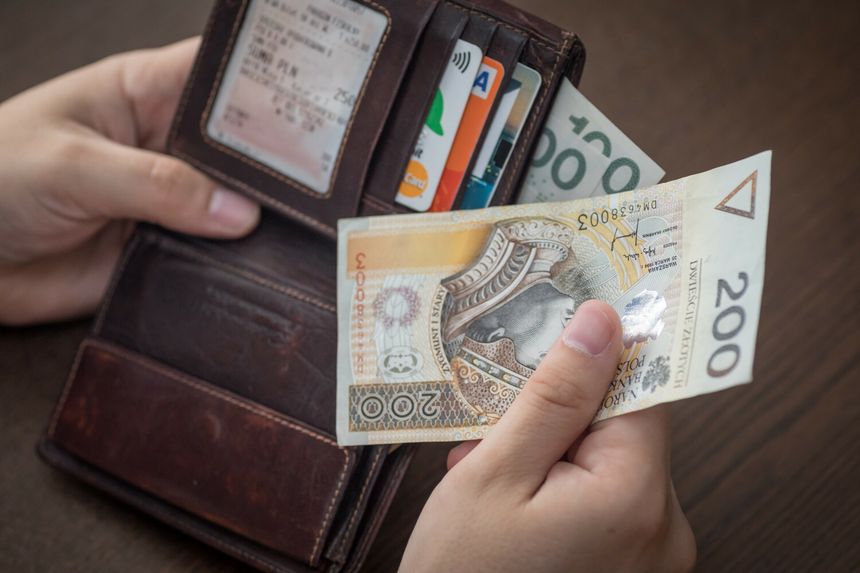 Zdjęcie przedstawia dłoń trzymającą banknot 200 zł w portfelu z kartami płatniczymi.