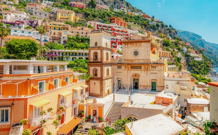 Widok na kolorowe budynki w Positano, Włochy, z kościołem i górzystym krajobrazem w tle.