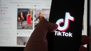 Obrazek przedstawia osobę trzymającą telefon z logo aplikacji TikTok na tle laptopa.