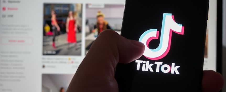 Obrazek przedstawia osobę trzymającą telefon z logo aplikacji TikTok na tle laptopa.