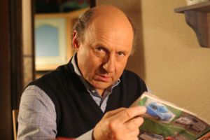 Mężczyzna w kamizelce siedzi przy stole, trzymając kolorowy magazyn z samochodami.