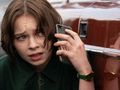 Młoda osoba z brązowymi włosami rozmawia przez telefon, wyglądając na zmartwioną.