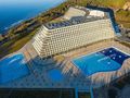 Nowoczesny budynek hotelowy przy plaży, w tle baseny i zieleń. Słoneczny dzień nad wodą.