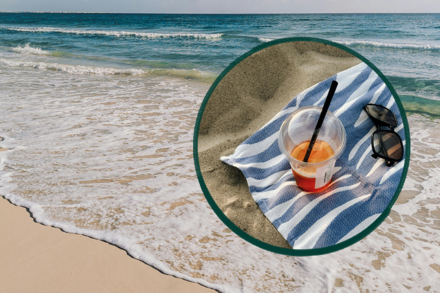 Kubek z zimnym napojem na plaży obok okularów przeciwsłonecznych i fali morskiej