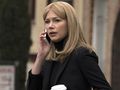 Kobieta w czarnym ubraniu, rozmawia przez telefon z kubkiem kawy w ręku.