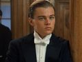 Młody mężczyzna w eleganckim garniturze z białą muszką, stojący obok drewnianej kolumny.