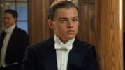 Młody mężczyzna w eleganckim garniturze z białą muszką, stojący obok drewnianej kolumny.