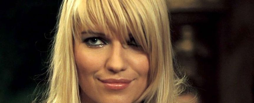 Kobieta z blond włosami, uśmiechająca się i mająca wyraziste makijażowe akcenty.