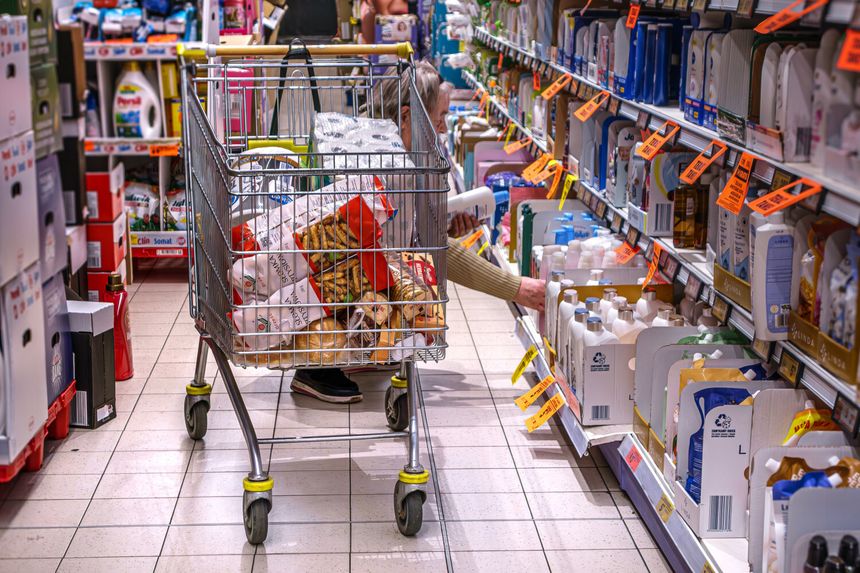 Zakupy w supermarkecie, w wózku jedzenie i środki czystości, klientka przeszukuje półki.