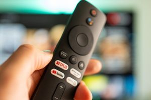 Pilot do telewizora trzymany w ręce, z przyciskami do różnych aplikacji streamingowych.