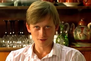 Mężczyzna z blond włosami siedzi w pomieszczeniu z zastawą stołową w tle.