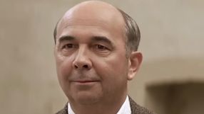 Mężczyzna z łysiną, w jasnej koszuli, uśmiechający się.