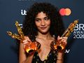 Kobieta z kręconymi włosami trzyma dwie statuetki na tle logo Brit Awards 2026.