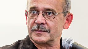 Mężczyzna z okularami, z siwymi włosami i wąsem, patrzy poważnie w stronę obiektywu.