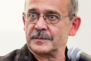 Mężczyzna z okularami, z siwymi włosami i wąsem, patrzy poważnie w stronę obiektywu.