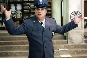 Mężczyzna w mundurze policjanta, z gestem wyrażającym zdziwienie, na tle biura.