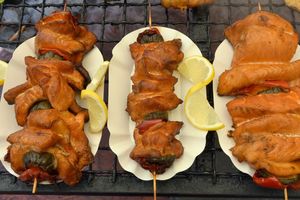 Trzy szaszłyki z grillowanym mięsem i warzywami, podane z plasterkami cytryny.