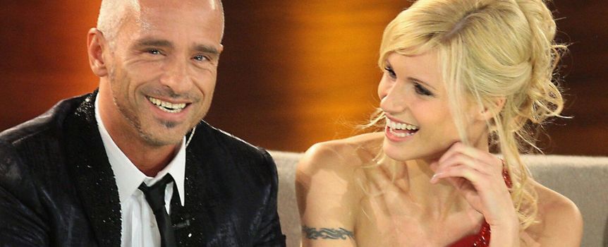 Na zdjęciu uśmiechnięta para w eleganckim stylu, siedzą na kanapie w studiu telewizyjnym.