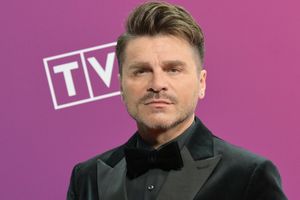 Mężczyzna w smokingu z bukietem, na tle purpurowego tła z logo TV.