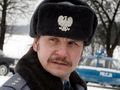 Mężczyzna w mundurze policjanta z czapką, z widocznym znakiem orła, na tle zimowego krajobrazu.