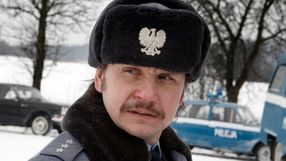 Mężczyzna w mundurze policjanta z czapką, z widocznym znakiem orła, na tle zimowego krajobrazu.