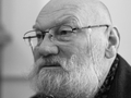Mężczyzna z siwą brodą i okularami, skupiony na rozmowie. Czarnobiałe zdjęcie.