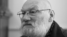 Mężczyzna z siwą brodą i okularami, skupiony na rozmowie. Czarnobiałe zdjęcie.