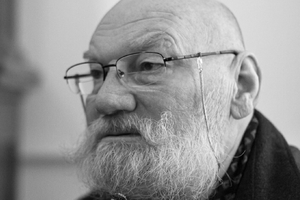 Mężczyzna z siwą brodą i okularami, skupiony na rozmowie. Czarnobiałe zdjęcie.