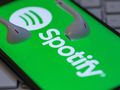 Zielone tło z logo Spotify i białymi słuchawkami. Telefon leży na klawiaturze.