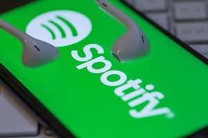 Zielone tło z logo Spotify i białymi słuchawkami. Telefon leży na klawiaturze.