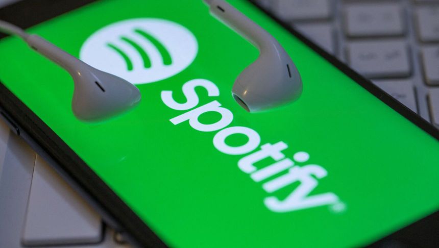 Zielone tło z logo Spotify i białymi słuchawkami. Telefon leży na klawiaturze.