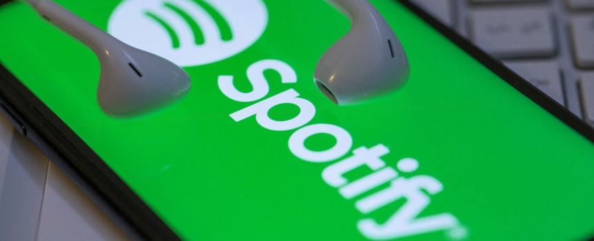 Zielone tło z logo Spotify i białymi słuchawkami. Telefon leży na klawiaturze.