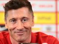 Robert Lewandowski uśmiechający się, siedzący w czerwonej koszulce, w tle kolorowe tło konferencji.