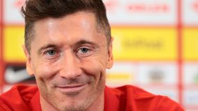 Robert Lewandowski uśmiechający się, siedzący w czerwonej koszulce, w tle kolorowe tło konferencji.