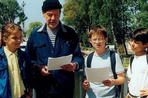 Grupa dzieci i dorosły mężczyzna na zewnątrz, wszyscy trzymają kartki papieru.