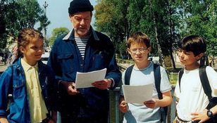 Grupa dzieci i dorosły mężczyzna na zewnątrz, wszyscy trzymają kartki papieru.