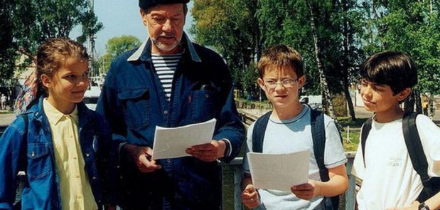 Grupa dzieci i dorosły mężczyzna na zewnątrz, wszyscy trzymają kartki papieru.
