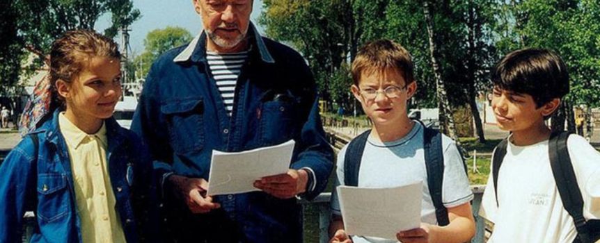Grupa dzieci i dorosły mężczyzna na zewnątrz, wszyscy trzymają kartki papieru.