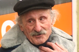 Na zdjęciu widoczny mężczyzna w czapce, z brodą i w futrzanej kurtce, na tle pomarańczowego tła.