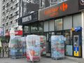 Widok sklepu Carrefour express z paletami napojów na zewnątrz, obok restauracji Brooklyn.