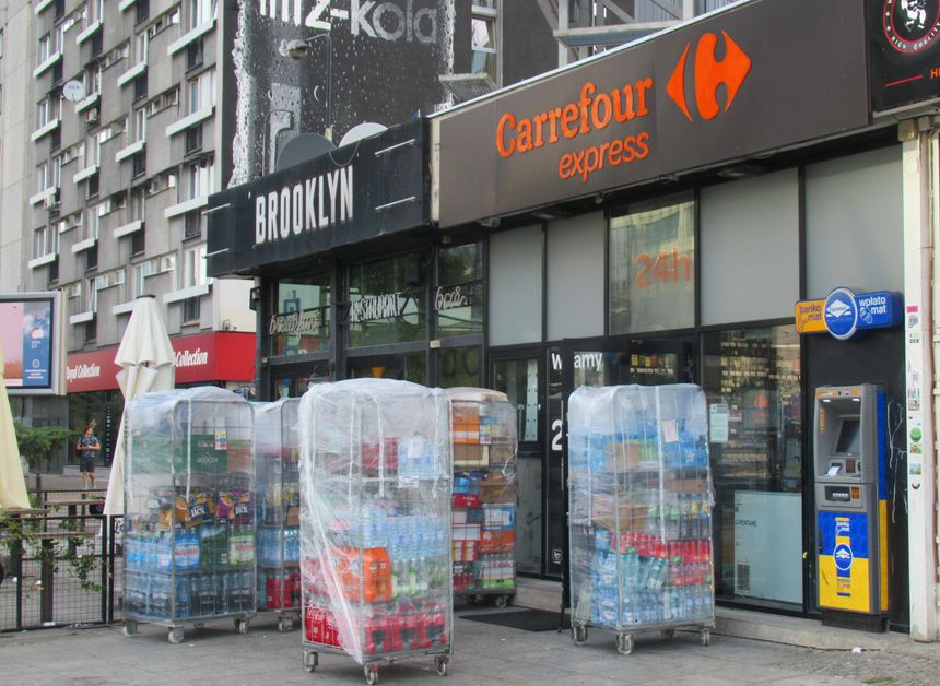 Widok sklepu Carrefour express z paletami napojów na zewnątrz, obok restauracji Brooklyn.