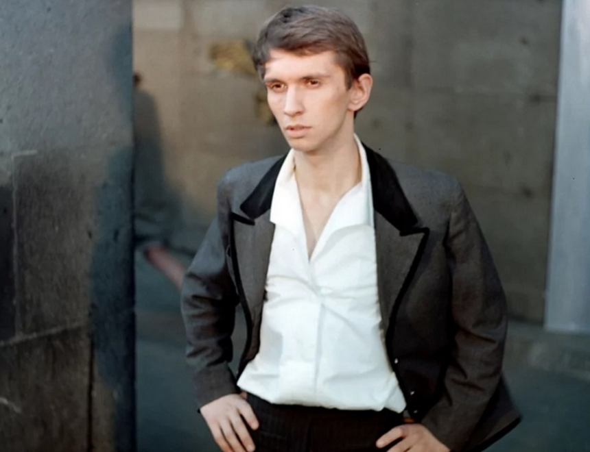 Młody mężczyzna w eleganckim garniturze, stoi przy ścianie, patrząc w dal.
